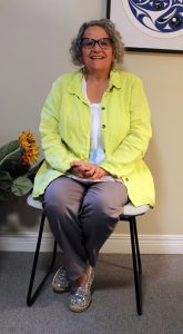 Barbara sitting in a chair in her clinic, wearing a yellow shirt.